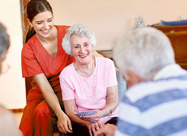 Senioren sitzend spielend und lachend am Tisch mit Pflegerin