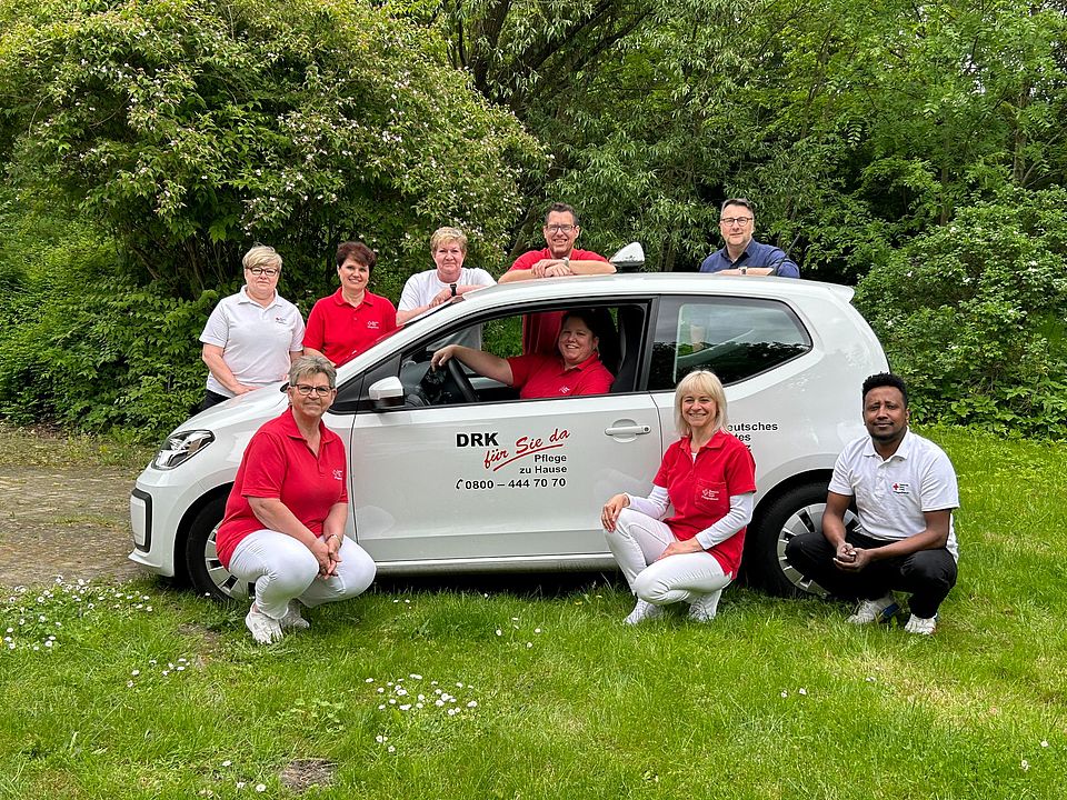 Team der ambulanten Pflege stehen um einen Dienstwagen