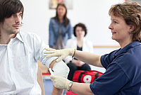 DRK-Dame verbindet den Arm eines Mannes im Erste Hilfe Kurs
