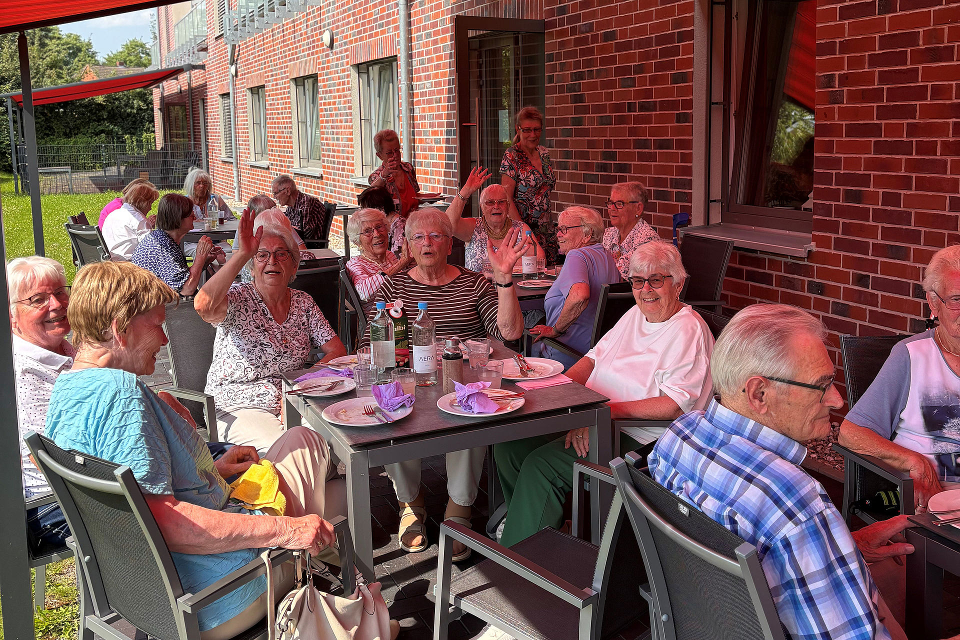 Eine fröhliche Gruppe SeniorInnen sitzt an Tischen auf der Terrasse unter der Markiese